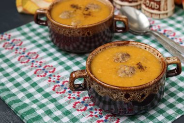 Karanlık bir arka plan üzerinde damalı peçete üzerinde kase kabak çorbası.