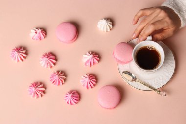 Kremalı kurabiye ve macaroons pembe arka plan, fincan kahve ve kadınların elleri üzerinde