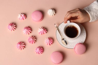 Kremalı kurabiye ve macaroons pembe arka plan, fincan kahve ve kadınların elleri üzerinde