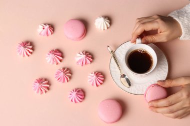 Kremalı kurabiye ve macaroons pembe arka plan, fincan kahve ve kadınların elleri üzerinde
