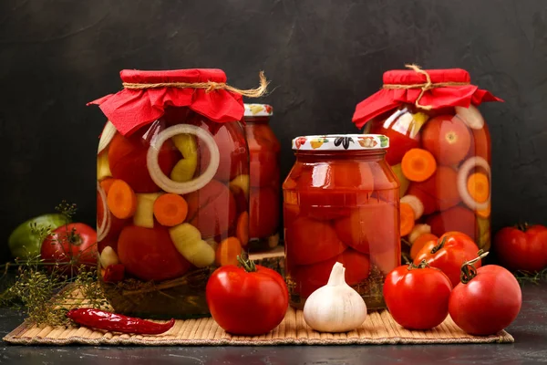 Varios frascos de tomates se encuentran en una mesa, sobre un fondo oscuro — Foto de Stock