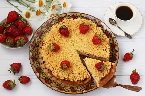 Curd cake with strawberries with a cut piece of cake, cup of coffee and a bowl with strawberries, Top view, on white background