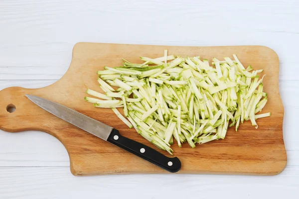 Zucchini, tăiate în benzi subțiri, aranjate pe o placă de lemn pe fundal alb, vedere de sus, de asemenea, există un cuțit următor — Fotografie, imagine de stoc