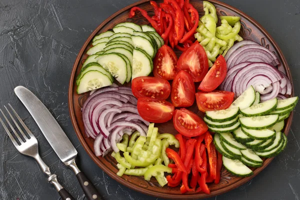トマト、赤タマネギ、コショウ、キュウリの健康的なサラダは、暗い背景のトップビューにプレート上に位置しています — ストック写真
