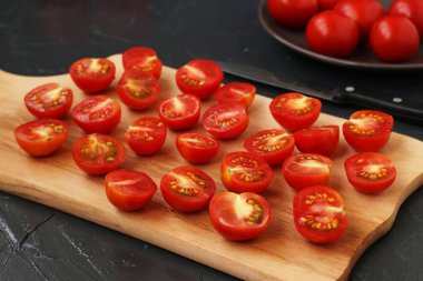 Kiraz domatesleri karanlık bir arka planda ahşap bir tahta üzerinde yarım kesilmiş