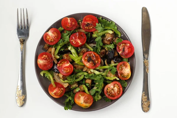 Salat mit Auberginen und Kirschtomaten auf dunklem Teller auf weißem Hintergrund, Draufsicht, Messer und Gabel auf dem Tisch — Stockfoto