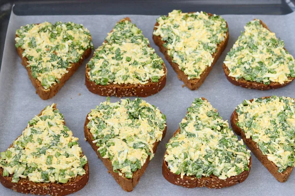 Sandvișuri fierbinți cu usturoi sălbatic, ceapă verde, ouă, brânză și pătrunjel situate pe hârtie pergament pe tava de copt — Fotografie, imagine de stoc