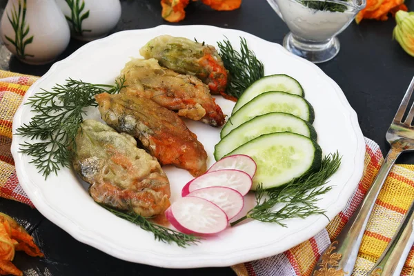 Flowers of zucchini, cooked in batter, slices of cucumbers and radishes on a plate