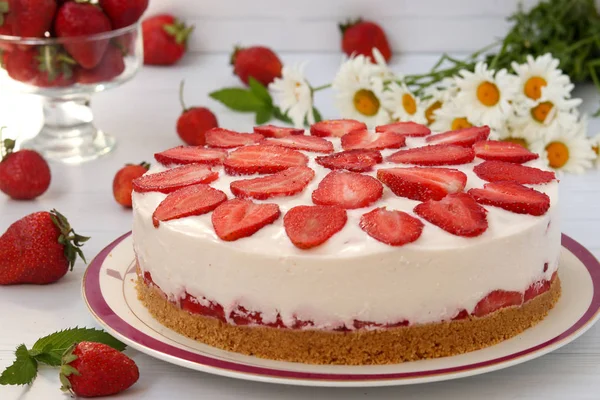 Un tort cu căpșuni fără coacere, cu o bază de biscuiți, este plasat orizontal pe o farfurie pe un fundal alb — Fotografie, imagine de stoc