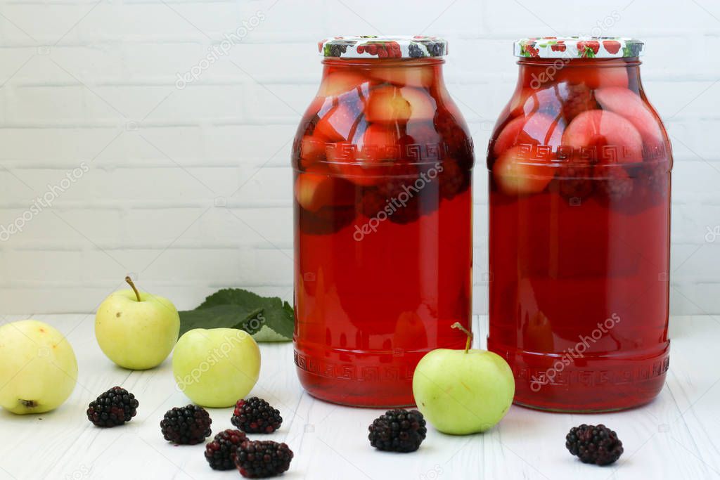 Compote of berries and apples in jars on a table on a white background, on the table there apples, blackberries. Free place for the inscription
