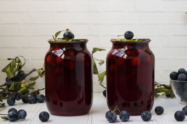 Compote with blackthorn in jars is located on a white background. Harvest for the winter clipart