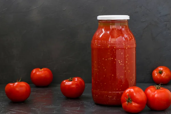 El jugo de tomate en un frasco colocado sobre una mesa sobre un fondo oscuro —  Fotos de Stock