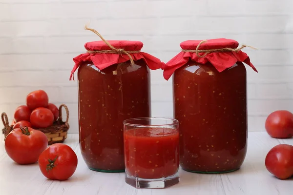 El jugo de tomate en latas y en un vaso está sobre la mesa sobre un fondo blanco —  Fotos de Stock