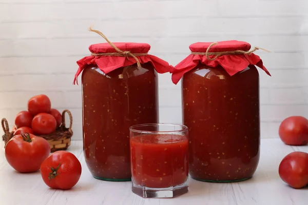 Tomato juice in cans and in a glass is on the table on a white background — Stock Photo, Image