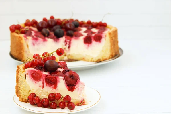Торт з ягодами розташований на тарілці на білому тлі, шматочок торта на передньому плані — стокове фото