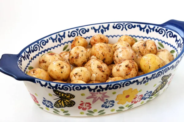 Молодой очищенный картофель в специях, приготовленных для жарки в керамической форме на белом фоне — стоковое фото