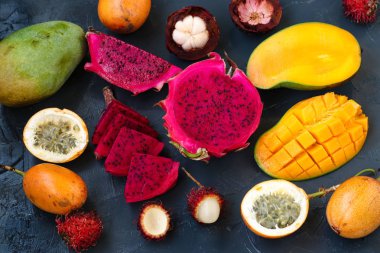 Tropikal meyveler: ejderha meyve, tutku meyve, mangosten, rambutan ve mango karanlık bir arka plan üzerinde yer almaktadır