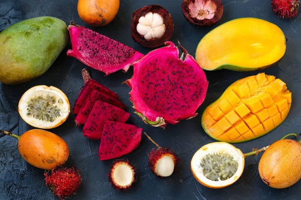 Tropical fruits: dragon fruit, passion fruit, mangosteen, rambutan and mangoes are located on a dark background