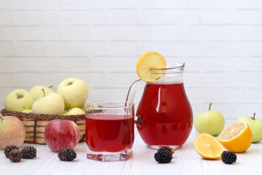 Bir sürahi içinde çilek ve elma kompostosu ve beyaz bir arka plan üzerinde bir masa üzerinde bir bardak. Fotoğrafta elma, böğürtlen ve limon var.