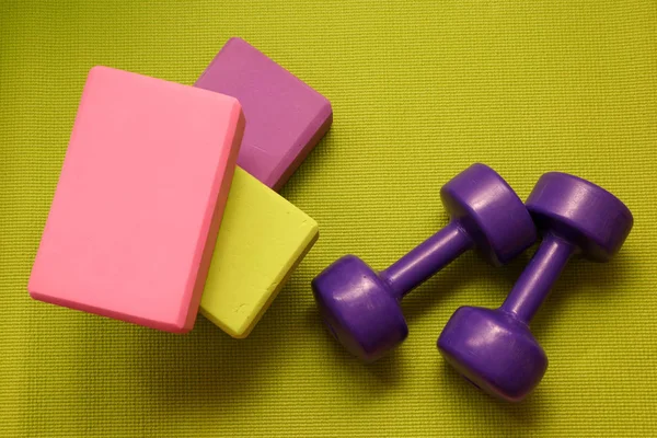Fitness tools - green, pink and purple cubes and dumbbells on a green mat, horizontal photo