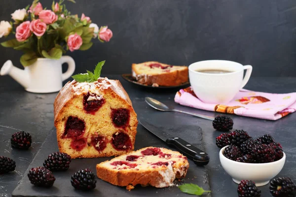 Cupcake with blackberries is located on a white plate on a dark background, section of the cake in the foreground — Stock Photo, Image