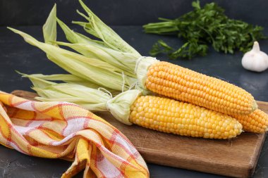 Taze, temizlenmiş Mısır koyu bir arka planda ahşap bir tahta üzerinde yer almaktadır, sarımsak yakın ve maydanoz bir demet