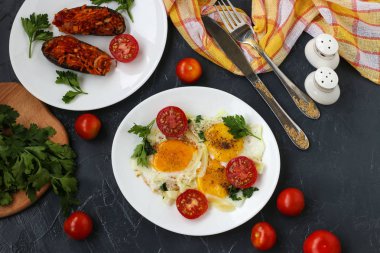 Kiraz domates ile Çırpılmış yumurta koyu bir arka plan üzerinde beyaz bir tabak üzerinde bulunan, fotoğraf orada pişmiş patlıcan, maydanoz, çatal bıçak takımı, üst görünümü