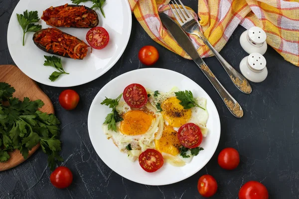 Kiraz domates ile Çırpılmış yumurta koyu bir arka plan üzerinde beyaz bir tabak üzerinde bulunan, fotoğraf orada pişmiş patlıcan, maydanoz, çatal bıçak takımı, üst görünümü