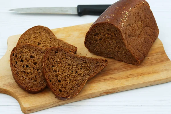 Sandviçler için siyah ekmek beyaz bir arka plan üzerinde ahşap bir tahta üzerinde dilimler halinde kesilir, fotoğraf bir bıçak var