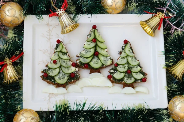 Новогодние бутерброды из черного хлеба, сыра и огурцов в виде новогодней елки, украшенные ягоды, расположенные на белой тарелке, вид сверху — стоковое фото