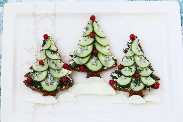 Sanduíches de Ano Novo de pão preto, queijo e pepinos na forma de uma árvore de Natal, bagas decoradas, localizadas em uma placa branca, vista superior — Fotografia de Stock