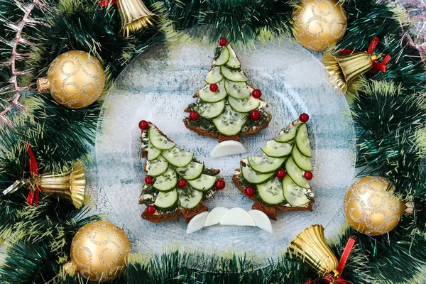 Новогодние бутерброды из черного хлеба, сыра и огурцов в виде рождественской елки, украшенные ягоды, расположенные на синем фоне, вид сверху — стоковое фото
