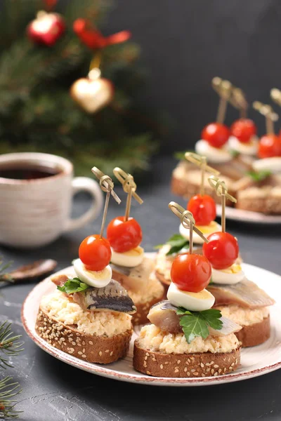 Canapes with salted herring, cheese, quail eggs and cherry tomatoes on rye croutons on the Christmas background — Stock Photo, Image