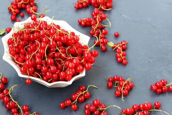 Red currant is arbitrarily located in a white plate on a dark background, horizontal photo