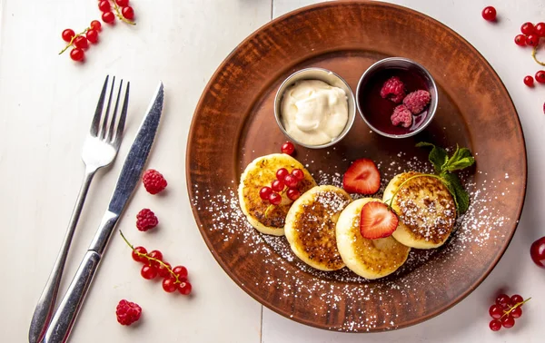 Cottage cheese pancakes, homemade traditional Ukrainian dish syrniki with berry sauce and sour cream on a brown plate on a white background, horizontal photo — Stock Photo, Image