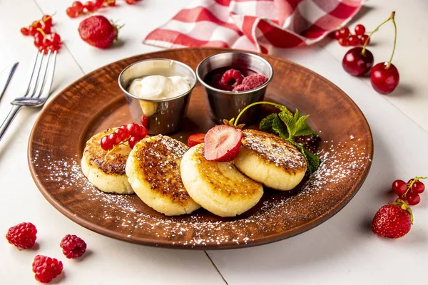 Cottage cheese pancakes, homemade traditional Ukrainian dish syrniki with berry sauce and sour cream on a brown plate on a white background, horizontal — Stock Photo, Image