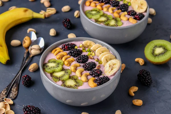 Healthy breakfast smoothie bowl with blackberries, bananas, cashews, kiwi and pistachios on a dark background, horizontal photo