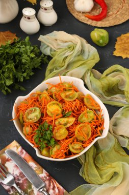 Koyu bir arka plan, dikey fotoğraf üzerinde beyaz bir salata kasesinde yeşil domates ve havuç ile Kore tarzı salata