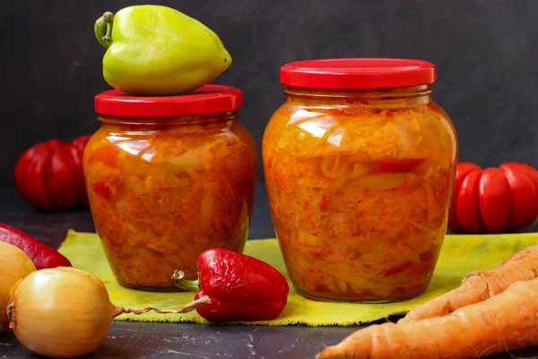 La ensalada vegetal de la zanahoria, los pimientos, la cebolla y los tomates para el invierno se encuentra sobre la mesa sobre el fondo oscuro —  Fotos de Stock