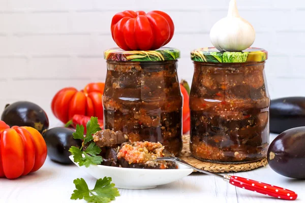 Berenjenas en salsa aguda de pimienta, tomates y ajo en frascos sobre la mesa, cosecha para el invierno — Foto de Stock