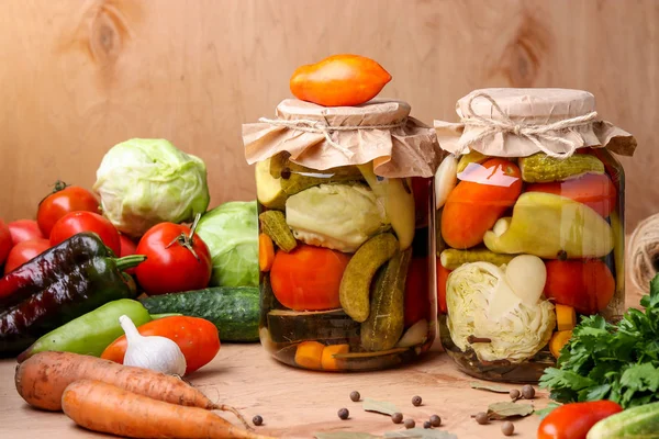 Blandade inlagda grönsaker i burkar: gurkor, tomater, kål, zucchini och paprika med vitlök, dill och lagerblad i burkar på en trä bakgrund, horisontell bild — Stockfoto