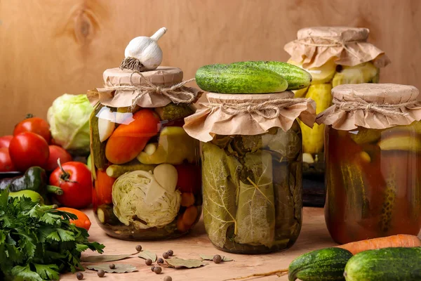 Diferentes verduras marinadas: pepinos, tomates, col, calabacín y pimientos, pepinos en hojas de uva, pepinos con salsa de tomate de chile, pepinos con calabacín en frascos sobre fondo de madera —  Fotos de Stock