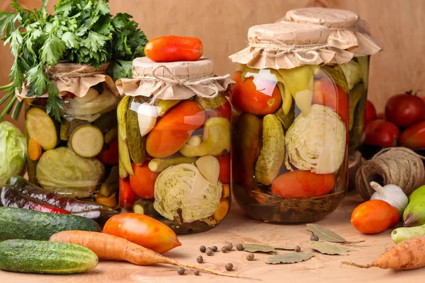 Vegetais conservados variados em jarros: pepinos, tomates, repolho, abobrinha e pimentas com alho, endro e folhas de louro em jarros em um fundo de madeira, estilo rústico — Fotografia de Stock