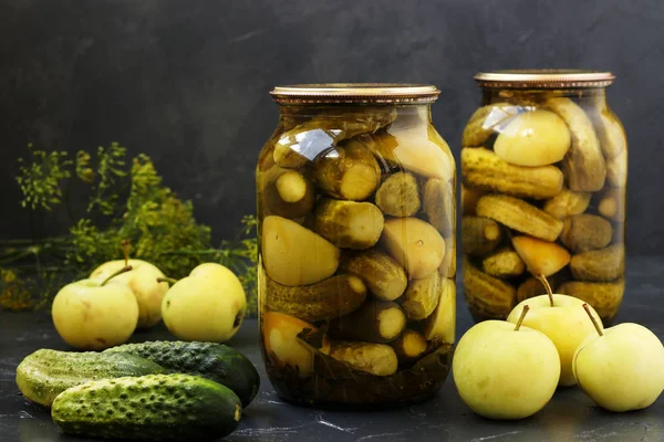 Concombres marinés avec des pommes dans des pots sont disposés sur un fond sombre, Récolte pour l'hiver, gros plan, photo horizontale — Photo