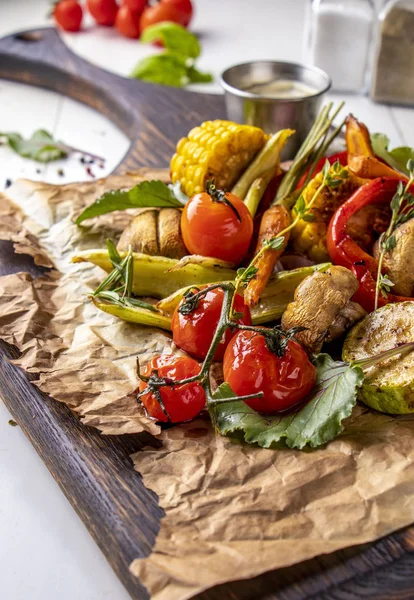 Menu Vegan Grill, Légumes grillés - courgettes, paprika, tomates cerises, maïs, carottes et champignons servis sur planche de bois à fond blanc, orientation verticale — Photo