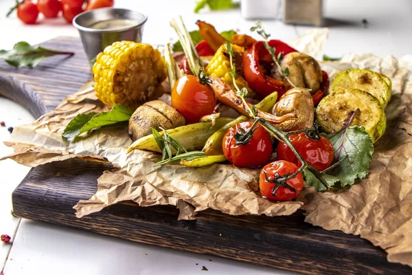 Vegan Grill menu, Grilled vegetables - zucchini, paprika, cherry tomatoes, corn, carrots and champignons served on wooden board at white background, horizontal orientation