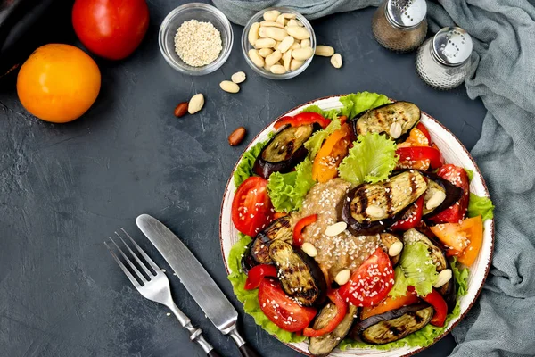 Salad with eggplant, tomato, paprika, lettuce, sesame and peanuts, top view on dark background, horizontal orientation — Stock Photo, Image