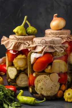 Çeşitli salatalık turşusu, patissons, domates, havuç, kabak, lahana ve biber kavanoz koyu bir arka plan, dikey yönelim