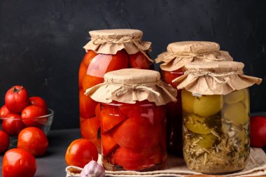 Konserve domates farklı türleri, domates yarım, cam kavanoz içinde horseradish ile yeşil domates koyu bir arka plan üzerinde uzun vadeli depolama için, yatay yönelim