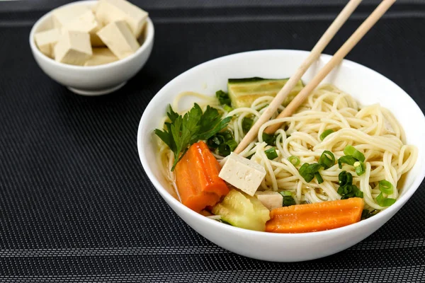 Supă asiatică tradițională cu brânză tofu, tăiței, morcovi și dovlecei pe fundal întunecat. Acest fel de mâncare conține de obicei bouillon și legume. — Fotografie, imagine de stoc